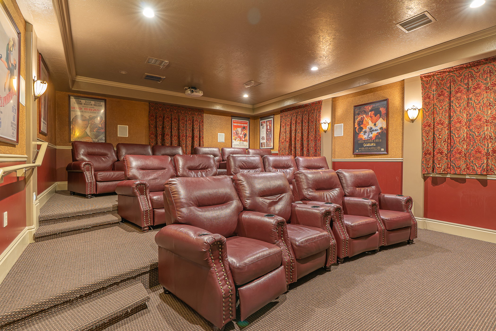 Dedicated home theater featuring tiered seating, individual leather recliners with cup holders, wall sconces, and recessed lighting
