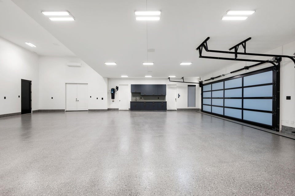 Spacious garage featuring a glass-paneled sectional door, light gray epoxy flooring, built-in dark cabinetry with a countertop, recessed square lighting, and white walls