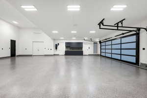 Spacious garage featuring a glass-paneled sectional door, light gray epoxy flooring, built-in dark cabinetry with a countertop, recessed square lighting, and white walls