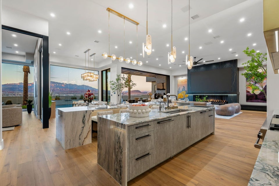 Gourmet kitchen featuring a large waterfall island with integrated sink, wood-finish flooring, recessed lighting, and a modern linear chandelier