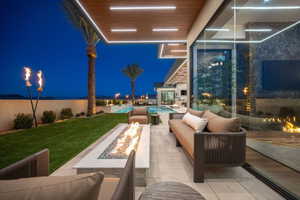 Expansive outdoor living area featuring a built-in linear fire pit, a covered patio with recessed lighting, and a manicured lawn