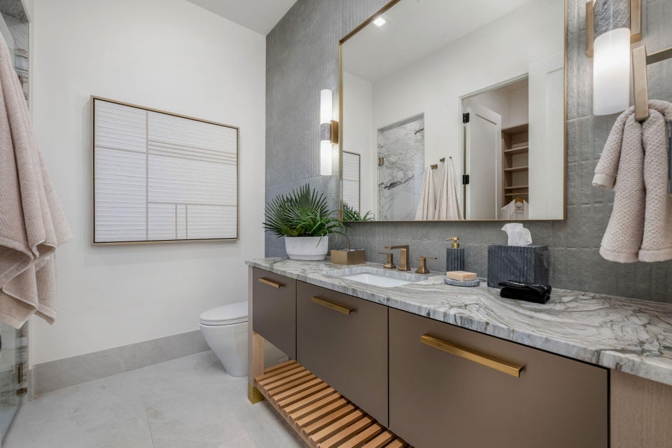 Bathroom vanity featuring a natural stone countertop with integrated sink, bronze-finish fixtures, and a large framed mirror