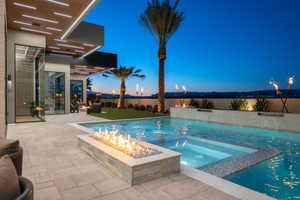 Expansive outdoor living area featuring a swimming pool with integrated spa, a linear fire feature, paver patio, and a grass lawn