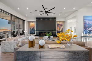 Open-concept living area featuring a sleek black fireplace, floor-to-ceiling sliding glass doors, recessed lighting, wood-finish flooring, and a modern ceiling fan