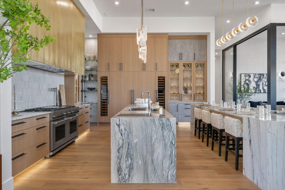 Gourmet kitchen featuring a large waterfall island with integrated sink, a second waterfall island with seating, a professional-grade range, full-height custom cabinetry, and wood-finish flooring