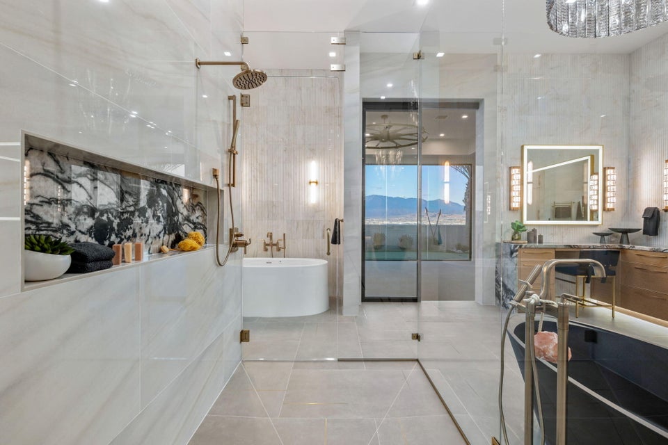 Contemporary bathroom featuring a spacious glass-enclosed shower with bronze fixtures, a built-in shelf with dark veined stone accent, a freestanding soaking tub, a dual vanity with illuminated mirror, and large format tile flooring