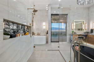 Contemporary bathroom featuring a spacious glass-enclosed shower with bronze fixtures, a built-in shelf with dark veined stone accent, a freestanding soaking tub, a dual vanity with illuminated mirror, and large format tile flooring