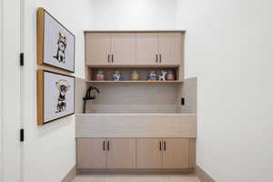 Dedicated utility space featuring a built-in wash basin with tiled surround, light wood-finish cabinetry, an open display shelf, and a matte black faucet