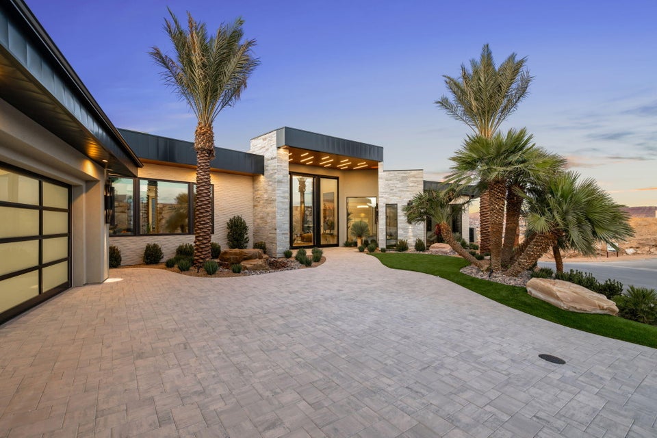 Contemporary exterior featuring a stone facade, a multi-pane glass garage door, a paver driveway, mature palm trees, and manicured landscaping