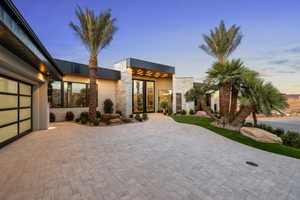 Contemporary exterior featuring a stone facade, a multi-pane glass garage door, a paver driveway, mature palm trees, and manicured landscaping