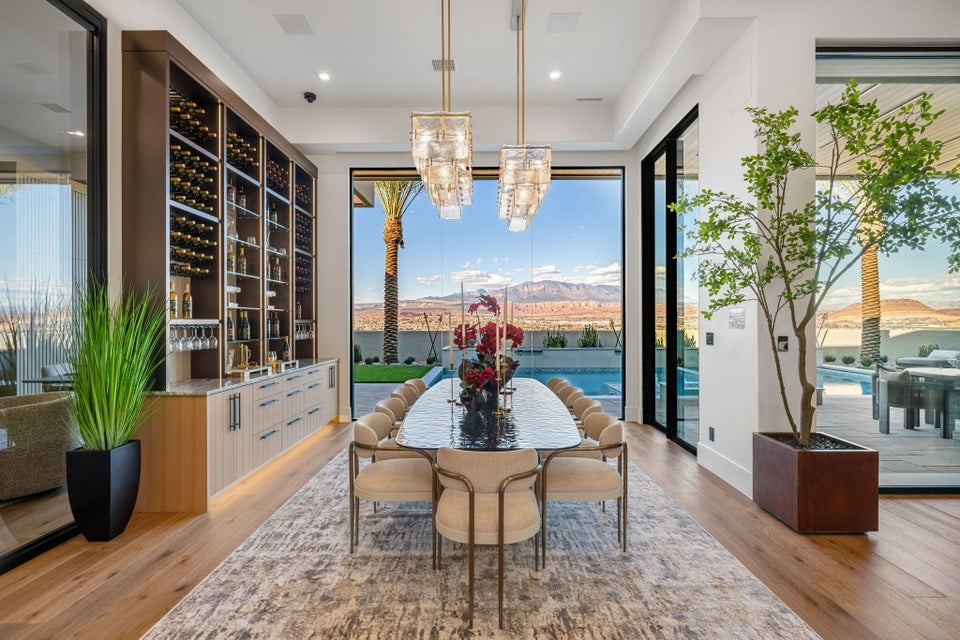 Spacious dining area featuring wood-finish flooring, a full-height built-in wine storage system, and two contemporary chandeliers