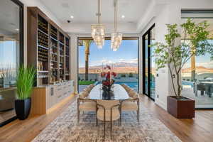 Spacious dining area featuring wood-finish flooring, a full-height built-in wine storage system, and two contemporary chandeliers