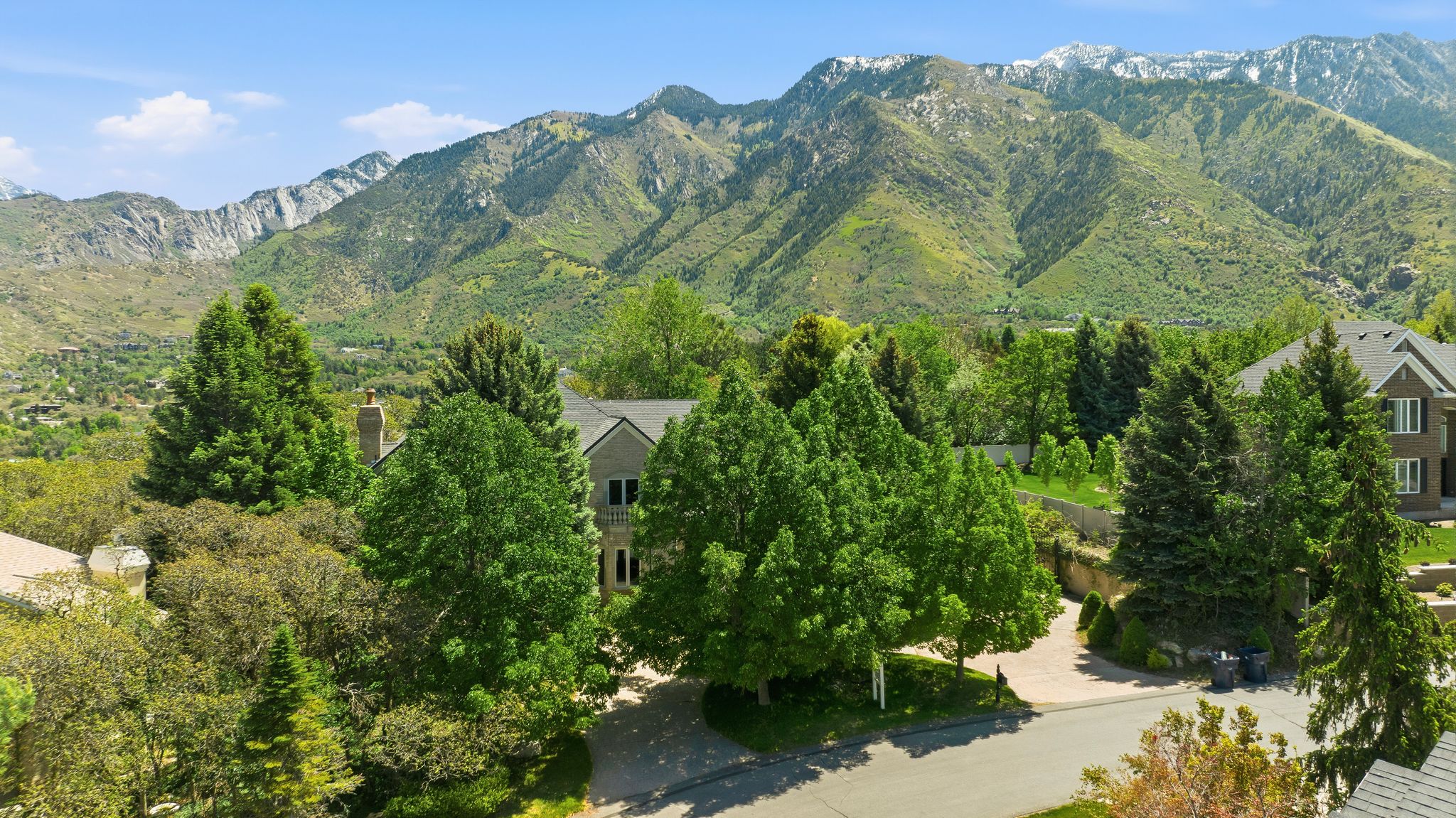Gable roofline residence with neutral siding, established trees, and a mountain backdrop