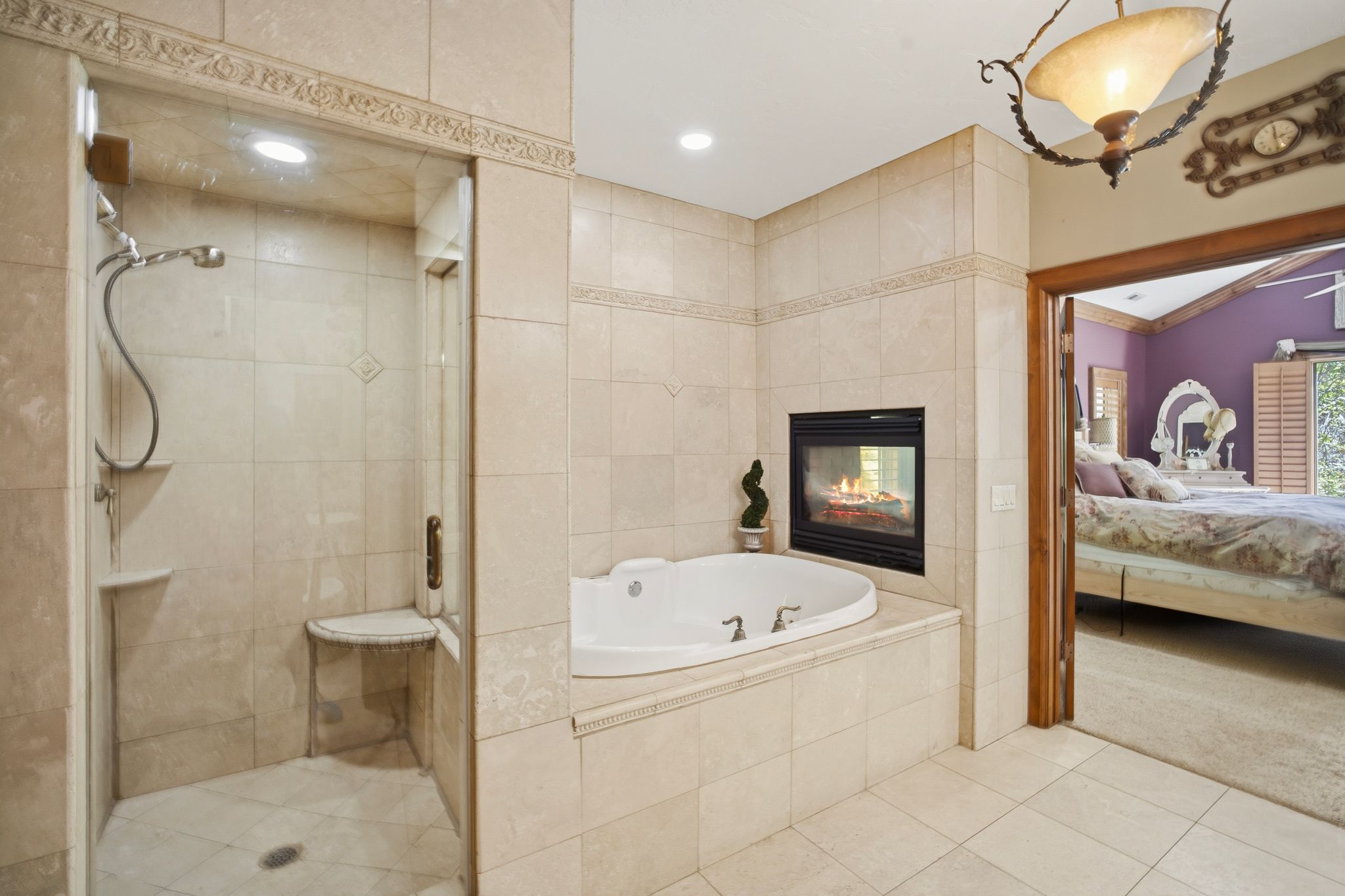 Spacious bathroom featuring a tiled walk-in shower with built-in bench, a jetted soaking tub, and an integrated fireplace