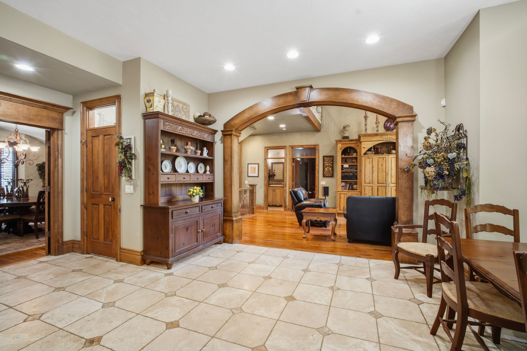 Spacious room featuring square tile flooring with decorative inserts, an expansive arched entryway with wood trim, and a framed doorway opening into an additional room