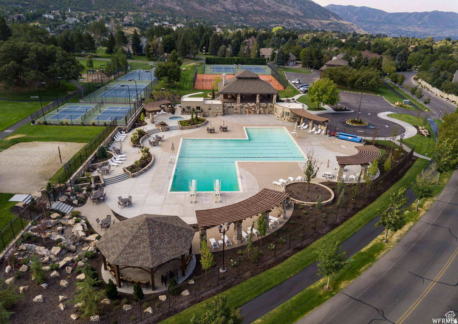 Expansive community recreation area featuring a large outdoor swimming pool with diving boards, multiple tennis courts, and a sand volleyball court