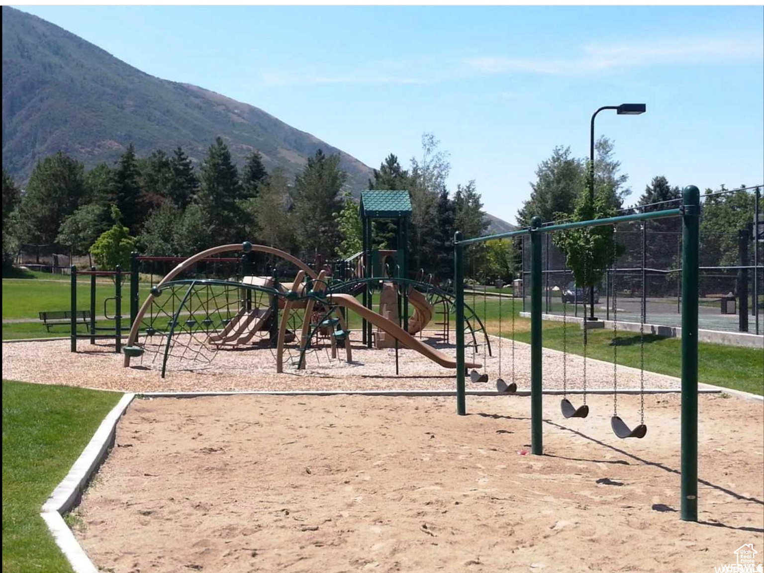 Expansive community playground featuring a multi-level play structure with slides and climbing nets, a four-swing set, and wood chip surfacing