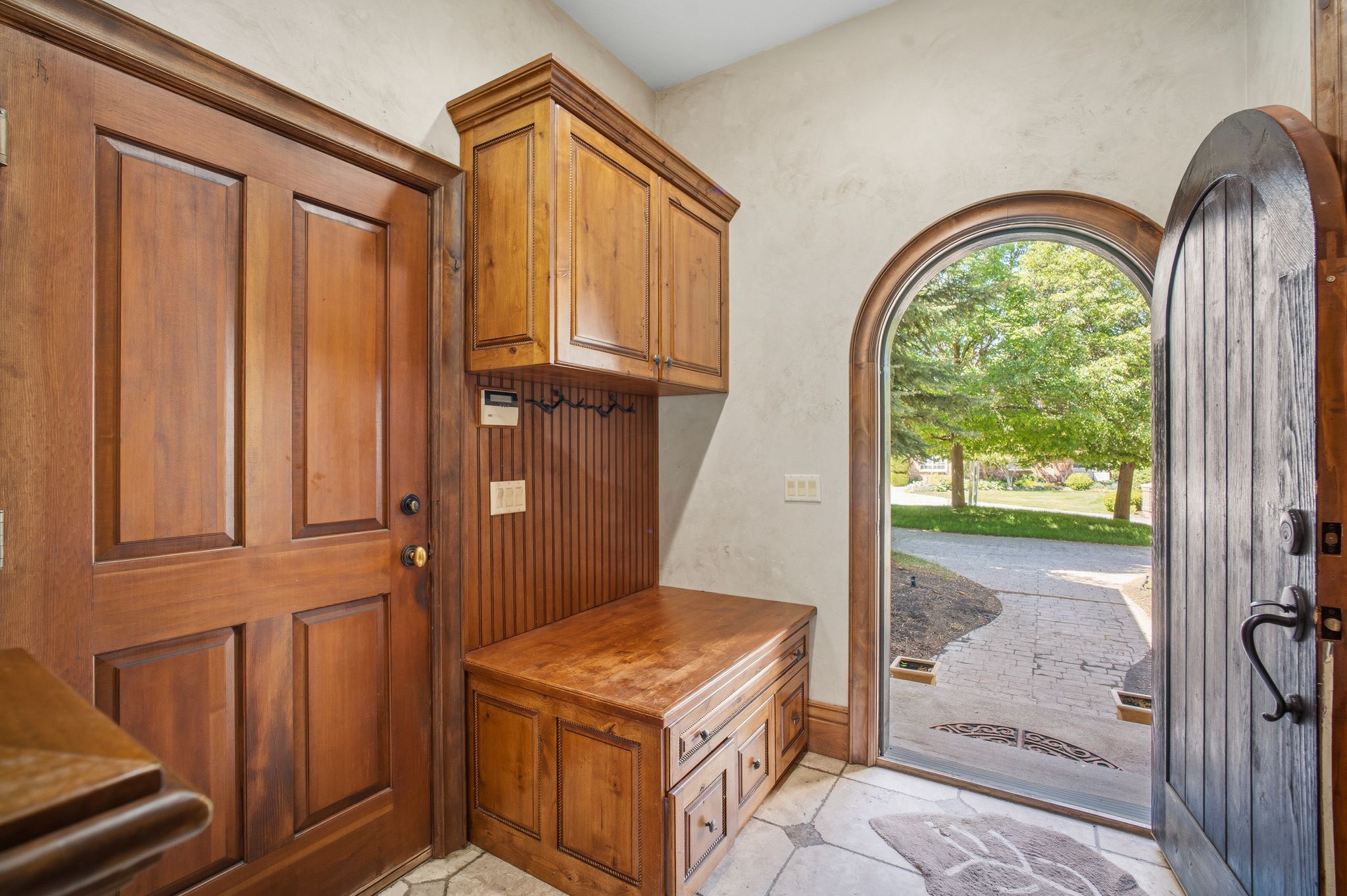 Entryway featuring an arched wood-paneled door, custom wood cabinetry with integrated bench seating, paneled interior door, and tiled flooring