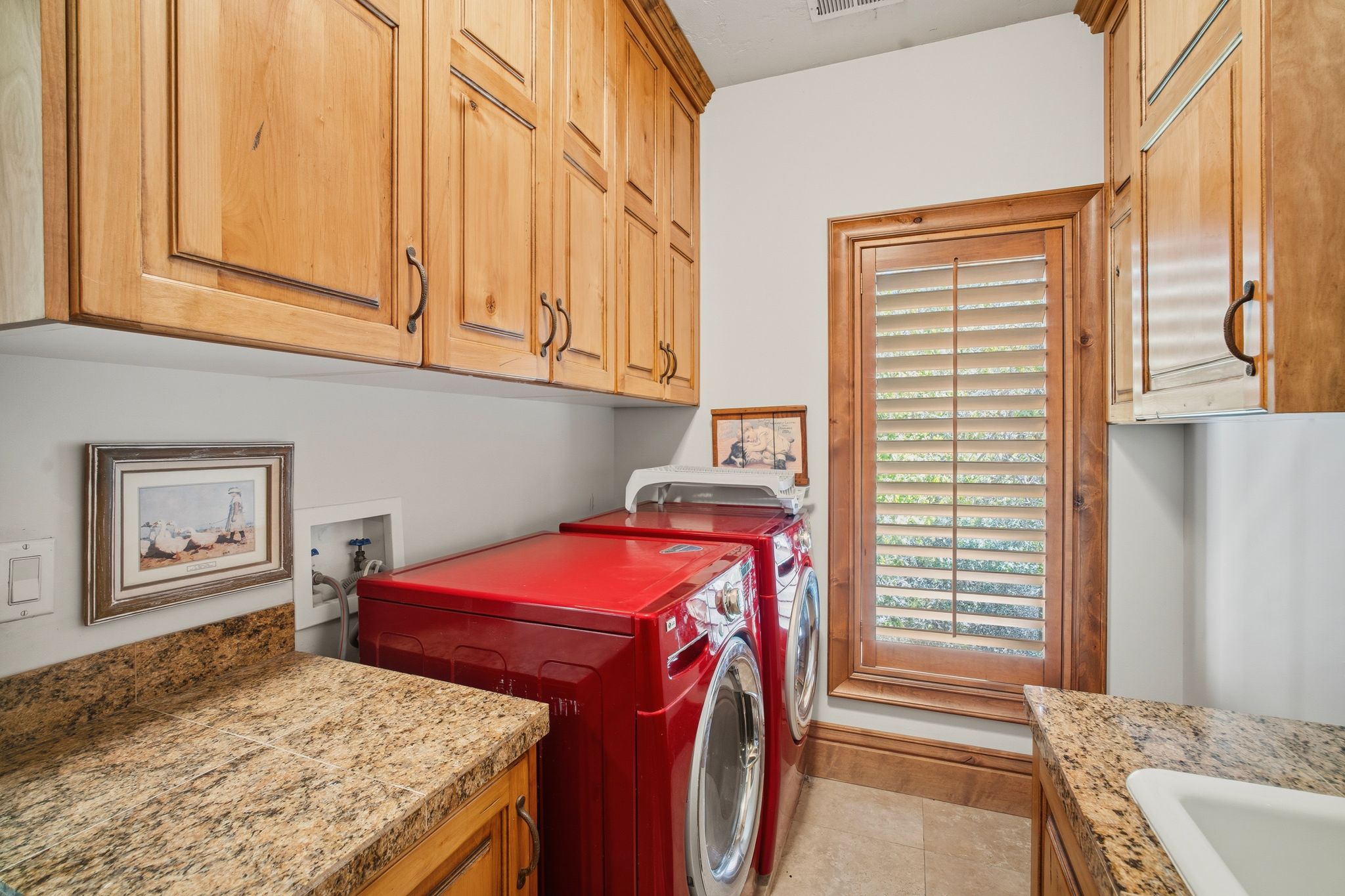 Laundry area featuring extensive wood cabinetry, light-toned countertops, and a window with wood plantation shutters