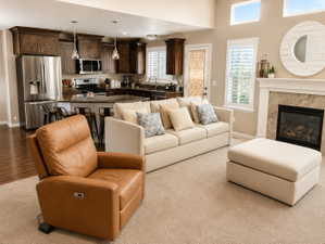 Open-concept living space featuring a gas fireplace with a stone surround, a kitchen with dark wood cabinetry, a stainless steel refrigerator, and pendant lighting