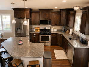 Gourmet kitchen featuring rich wood cabinetry, stainless steel appliances, granite countertops, a large island with seating, and wood-finish flooring