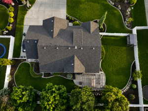 Expansive property featuring a multi-gabled roofline, concrete driveway, lush green lawns, perimeter fencing, and a rear patio with a pergola