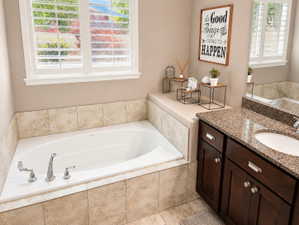 Built-in soaking tub with chrome fixtures, surrounded by neutral-toned tile and a window with white louvered shutters
