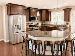 Kitchen featuring wood-finish flooring, dark wood cabinetry, stainless steel appliances, granite countertops, and a central island with seating