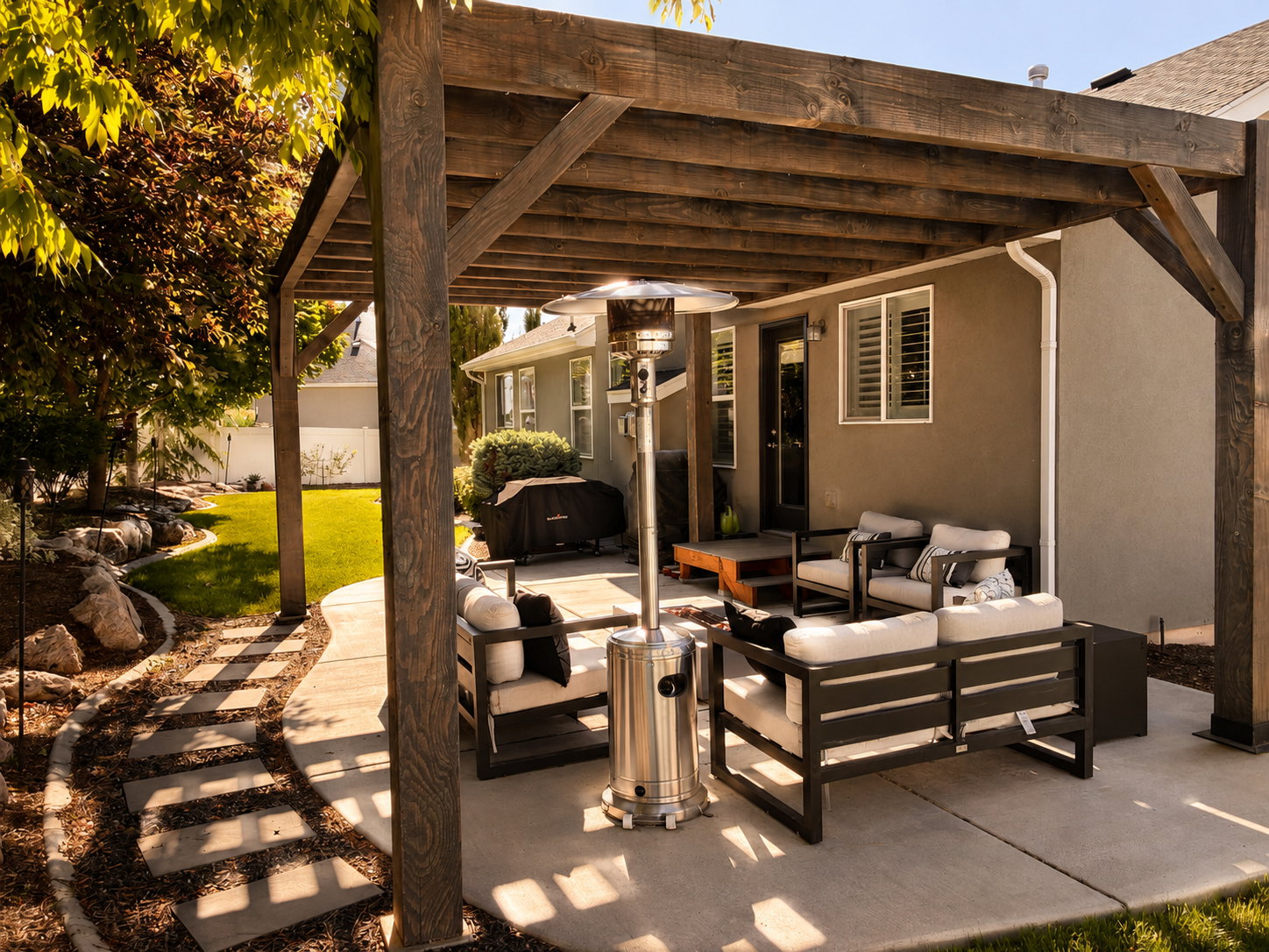 Expansive concrete patio featuring a wood pergola structure, a stepped garden path, and a manicured lawn