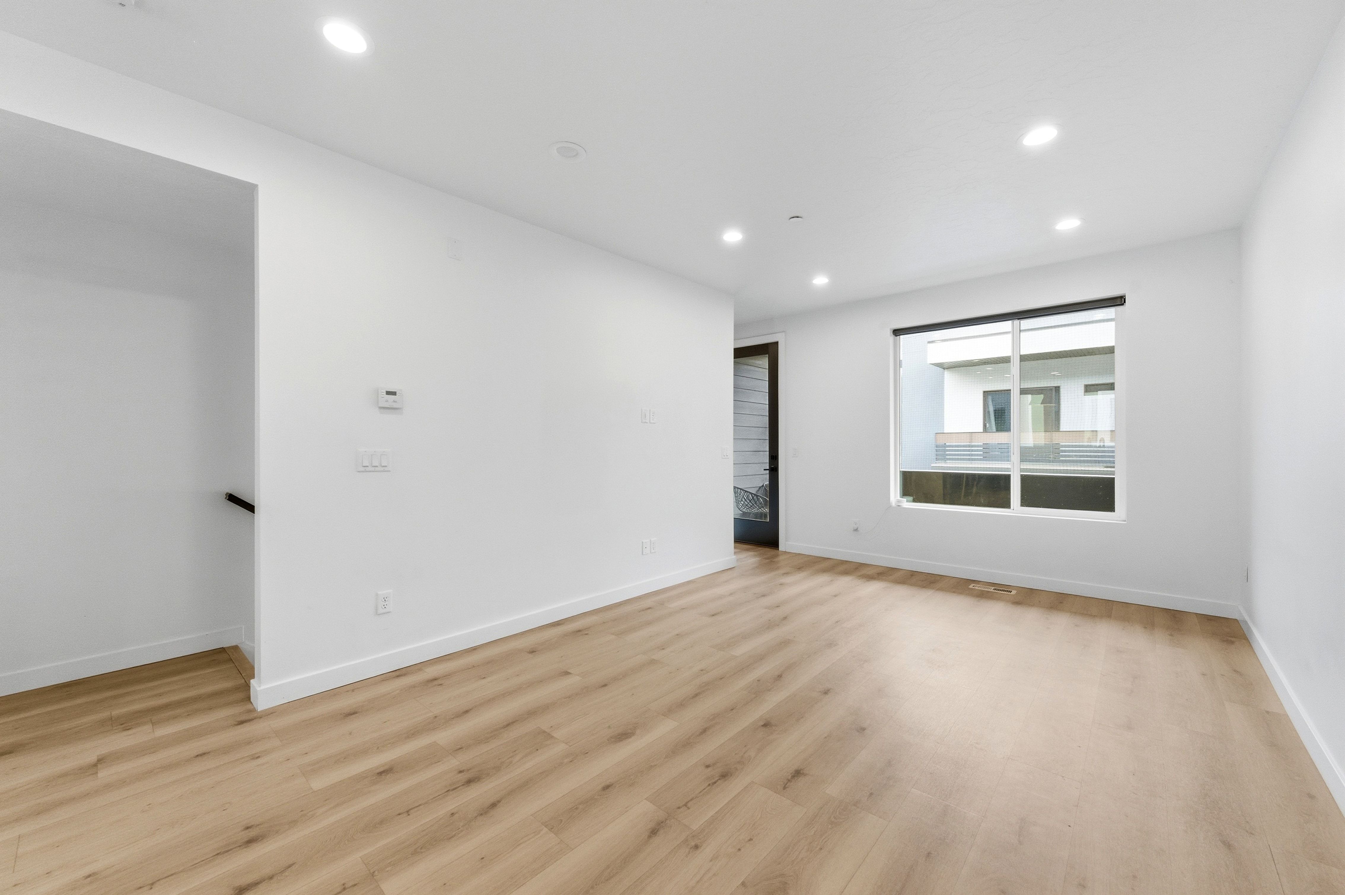Spacious interior featuring light wood-finish flooring, recessed lighting, white walls, and a large window with a dark frame