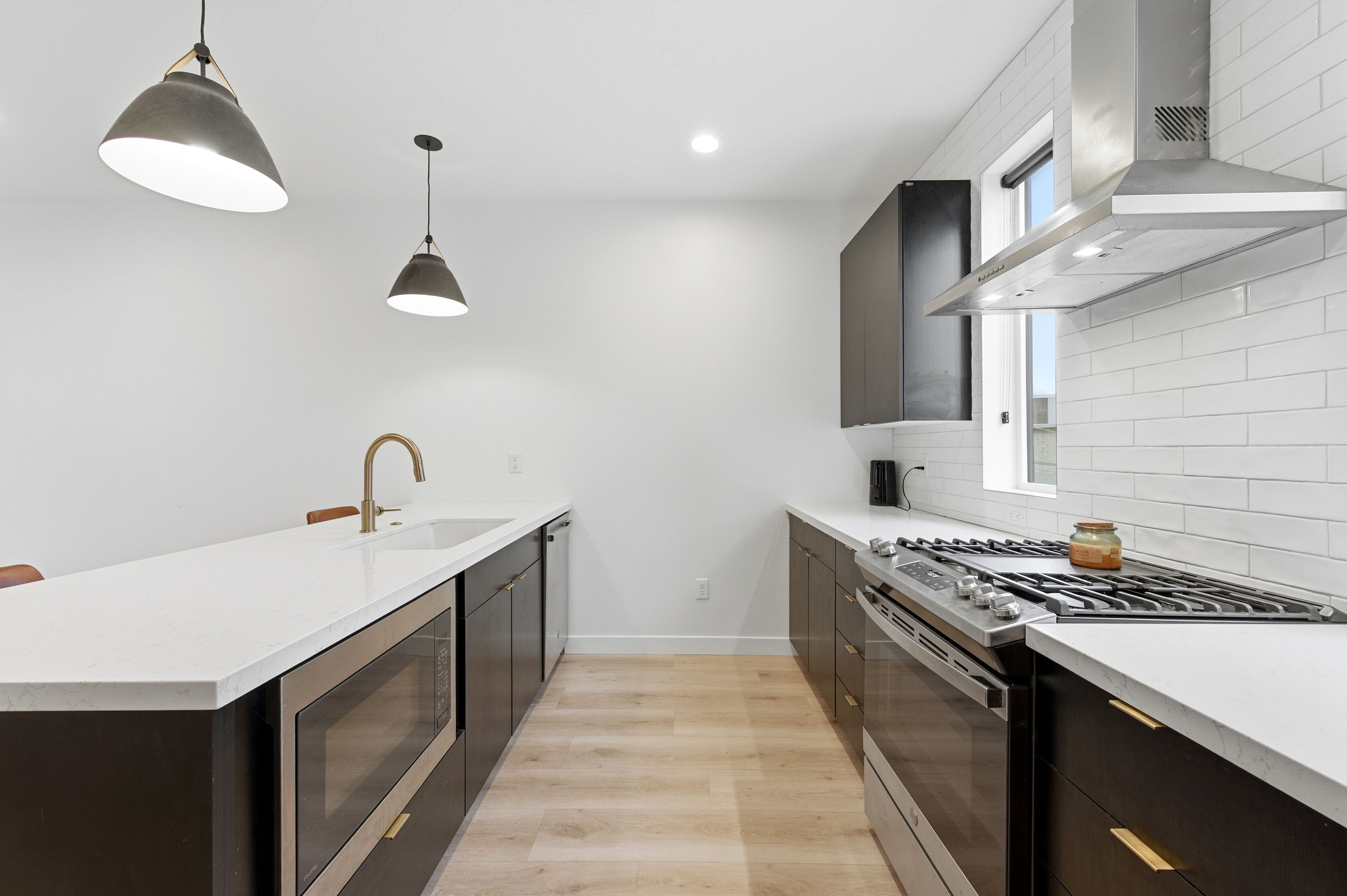 Kitchen featuring stainless steel appliances, dark cabinetry with gold-tone hardware, white countertops, and light wood-finish flooring