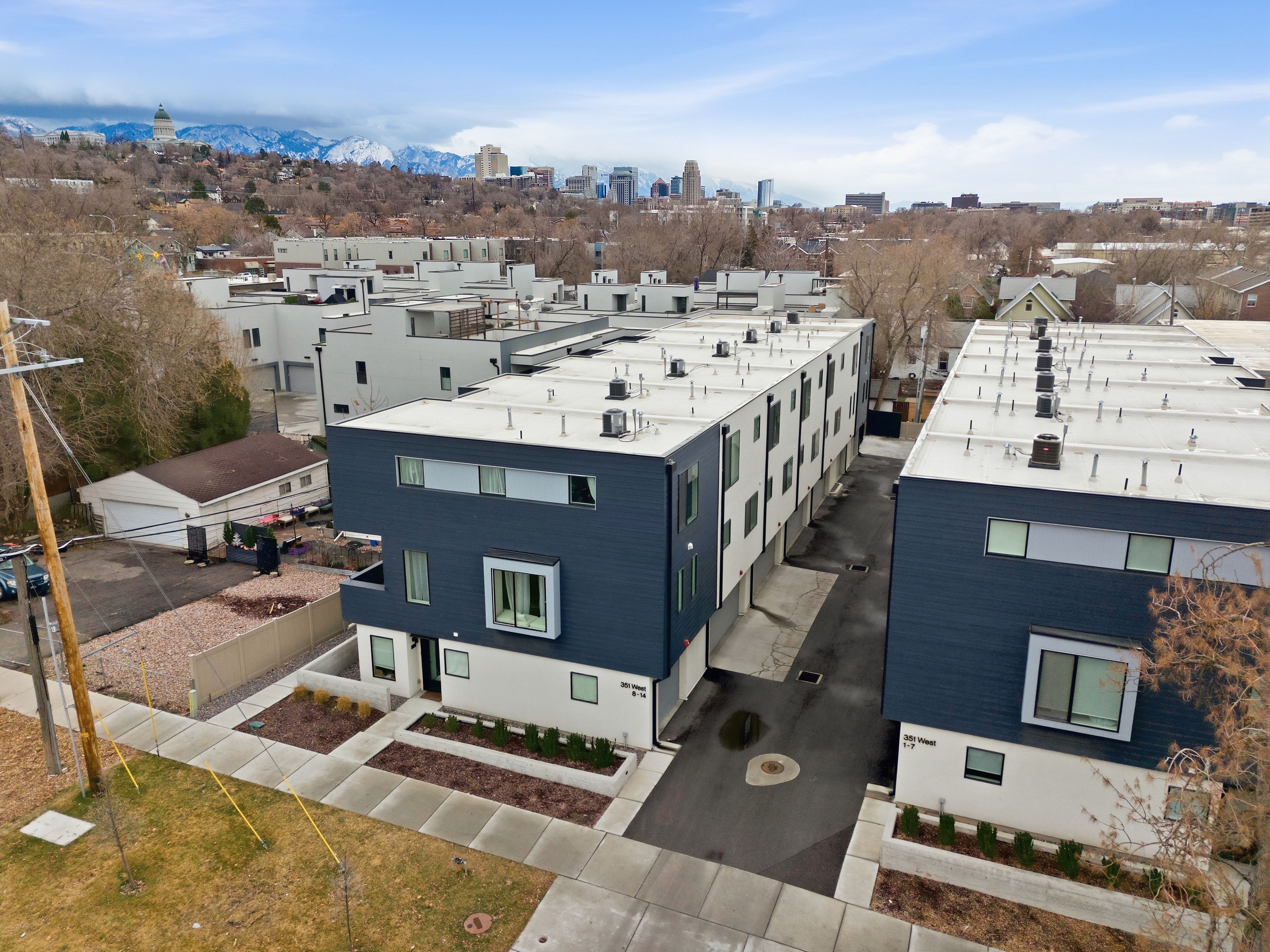 Modern townhome featuring a dark blue and white facade, flat roofline, integrated landscaping beds, and a paved driveway