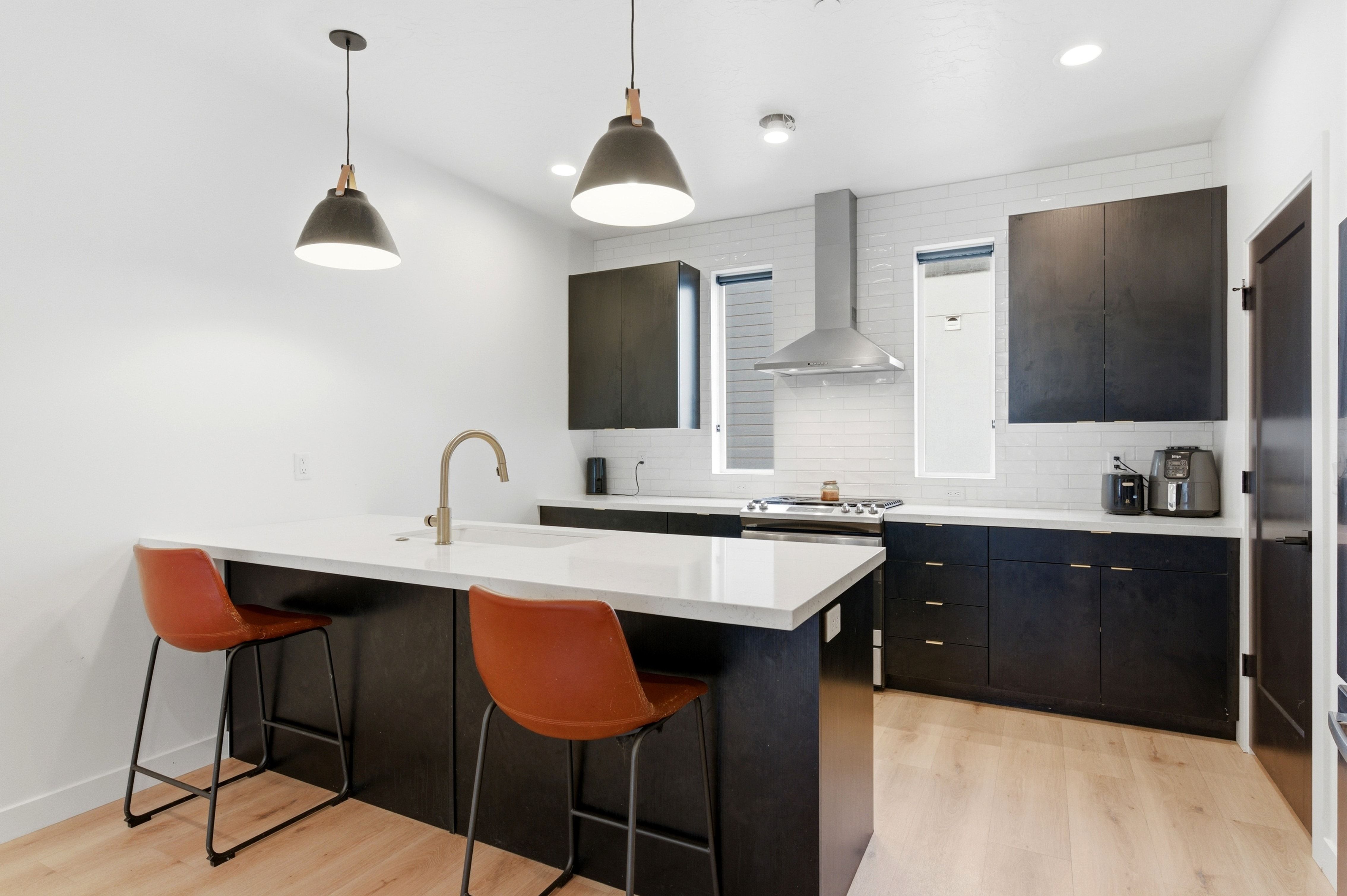 Contemporary kitchen featuring a large island with white countertops, dark cabinetry, stainless steel appliances, a subway tile backsplash, and light wood-finish flooring
