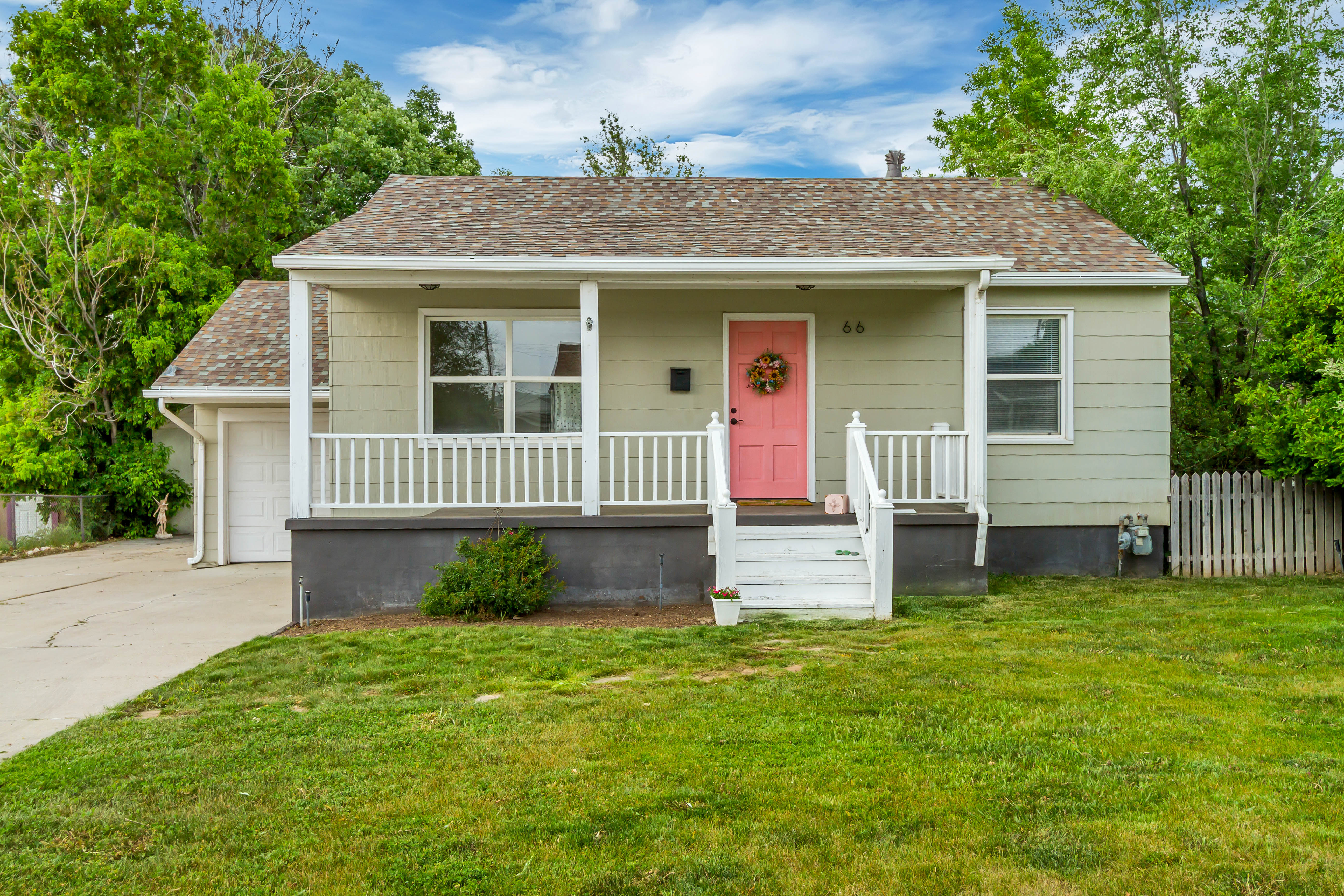 Charming single-story property featuring a covered porch, light green siding, and a vibrant pink front door