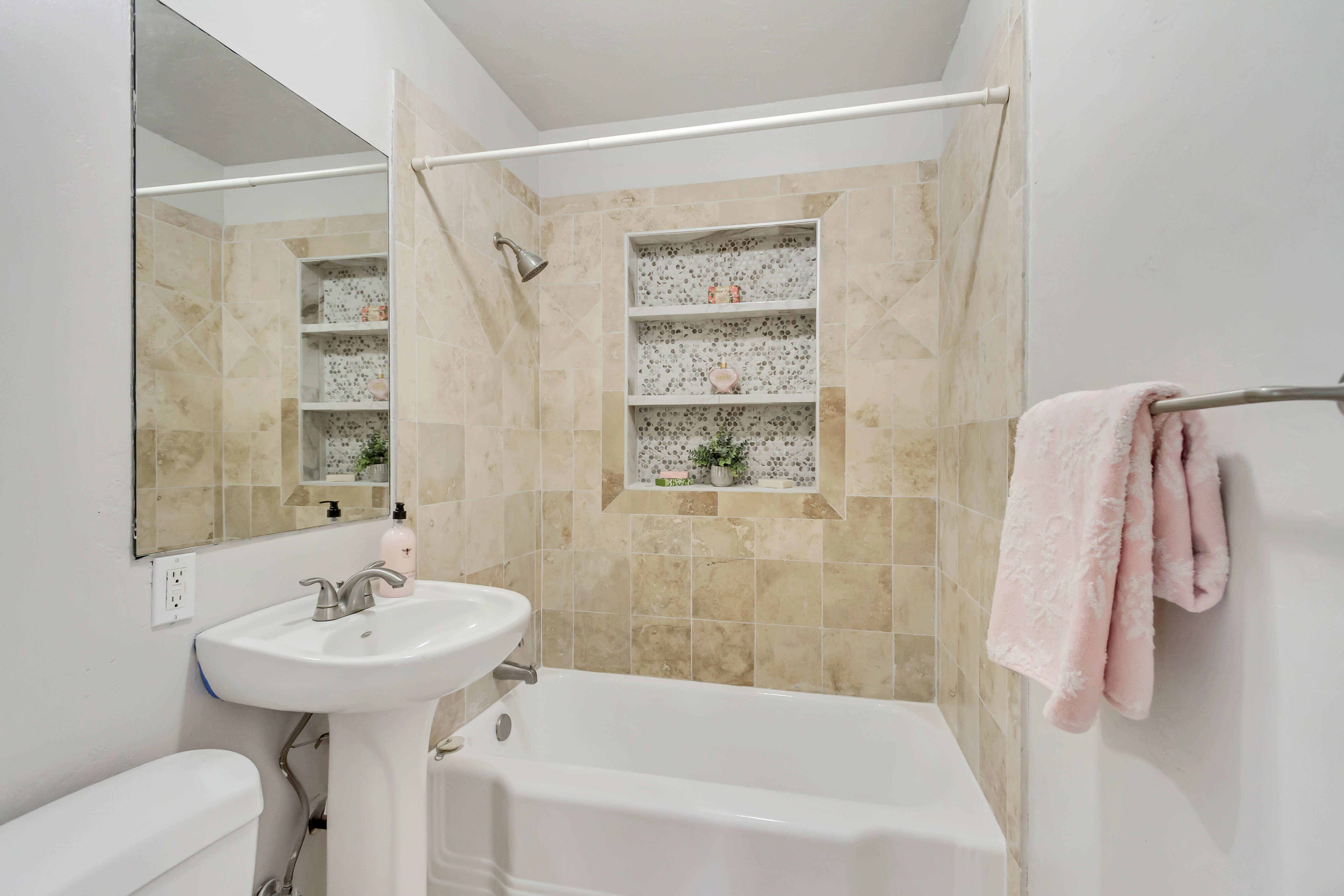 Bathroom featuring a pedestal sink with brushed nickel faucet, a shower/tub combination with subway tile surround, and an integrated shower niche with decorative tile