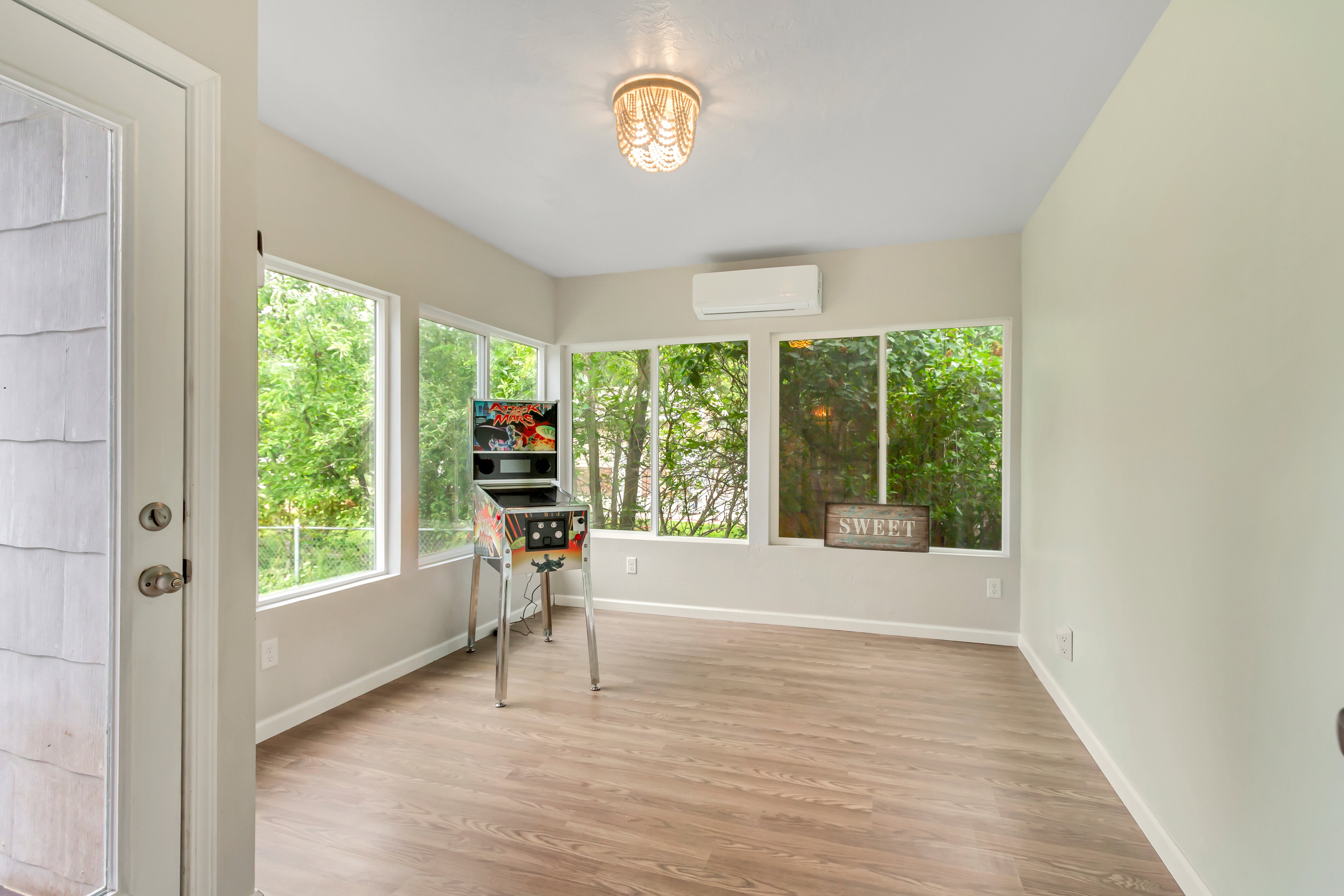 Sunroom featuring abundant natural light from multiple windows, wood-finish flooring, a contemporary chandelier, and a wall-mounted mini-split system