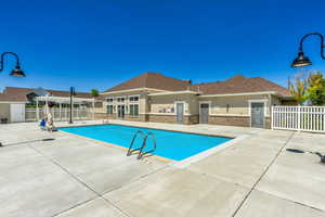 Community swimming pool with a concrete deck, white picket fencing, and an adjacent building featuring multiple entryways and a brown shingle roof