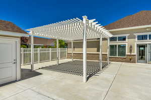 Spacious concrete patio featuring a white slatted pergola