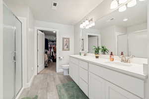 Double vanity with integrated sinks and white cabinetry, a glass-enclosed shower, a full-width mirror, and wood-finish flooring