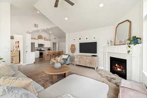 Spacious open-concept living area featuring vaulted ceilings, recessed lighting, and a white mantle fireplace with a tile surround