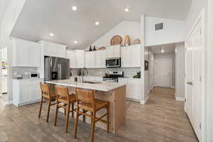 Open-concept kitchen featuring a large central island with seating, white shaker cabinetry, stainless steel appliances, and wood-finish flooring