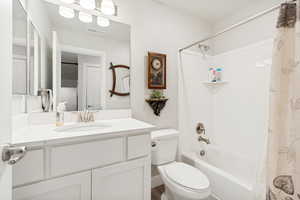 Bathroom featuring a white vanity with an undermount sink, a large mirror, a chrome faucet, a white toilet, and a white tub with shower