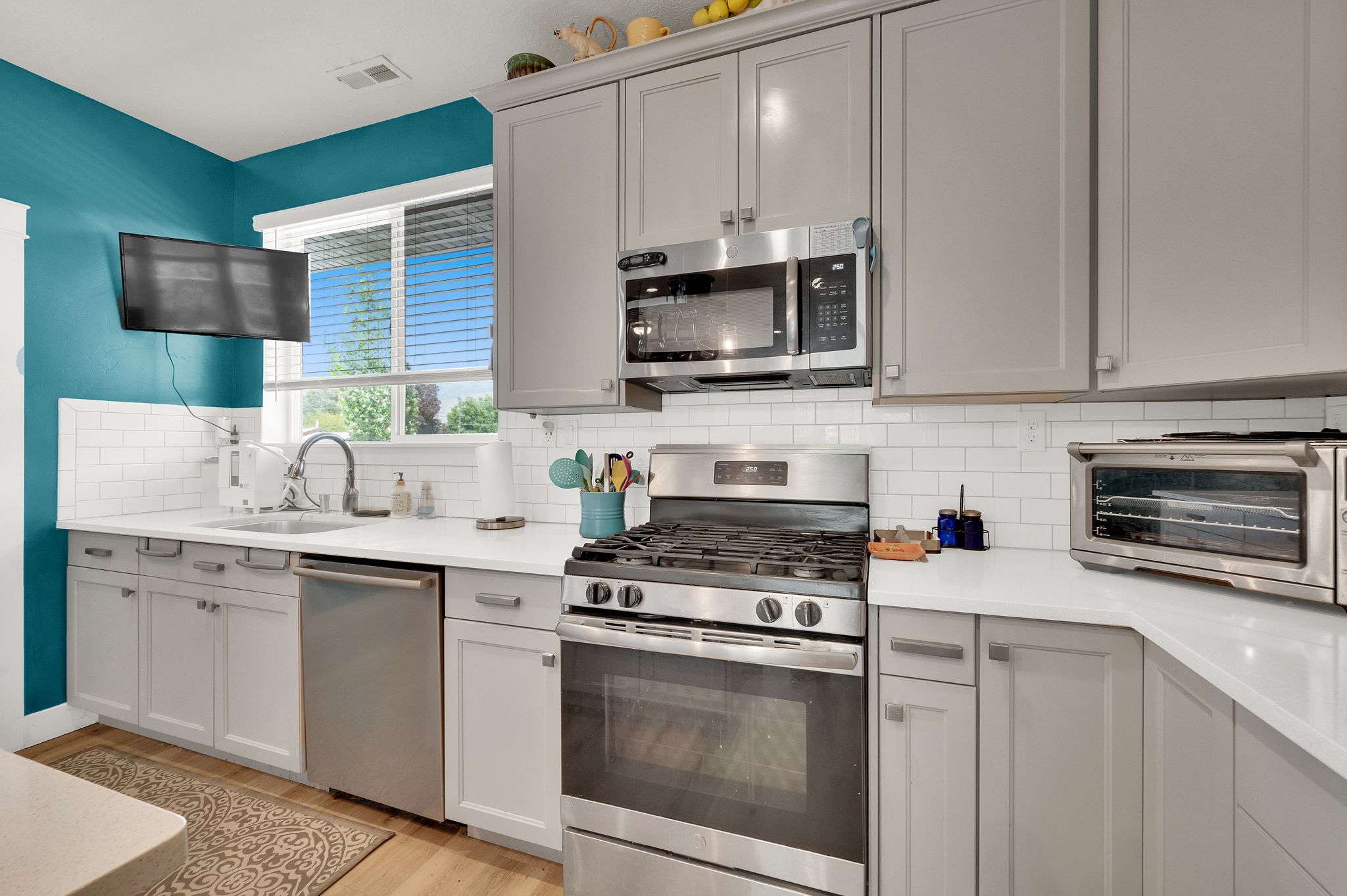 Modern kitchen featuring light gray cabinetry, stainless steel appliances, a white subway tile backsplash, and light-colored countertops