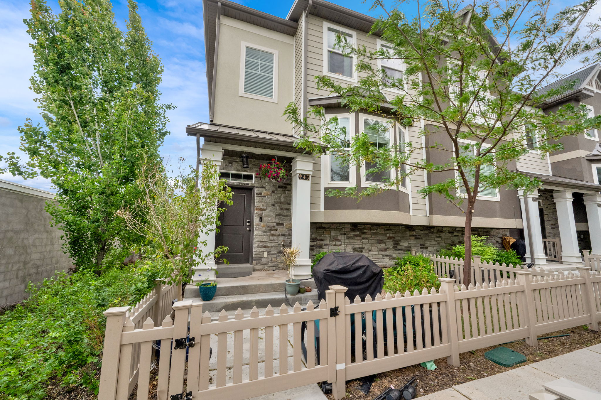 Contemporary townhome exterior featuring a neutral color palette, stone veneer accents, multiple window styles, a covered front entry, and a picket fence