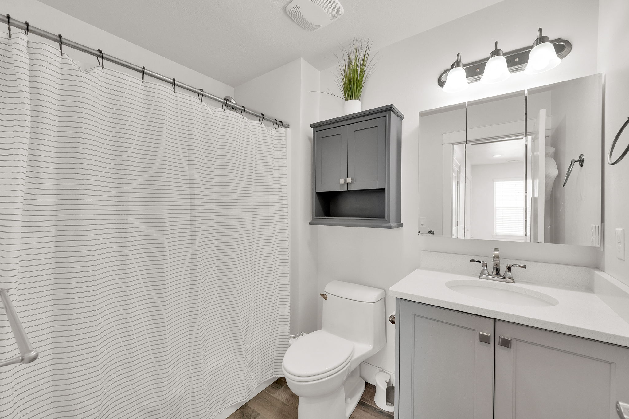 Bathroom featuring a shower with a grab bar, a built-in medicine cabinet, a vanity with a white countertop and gray cabinetry, and wood-finish flooring