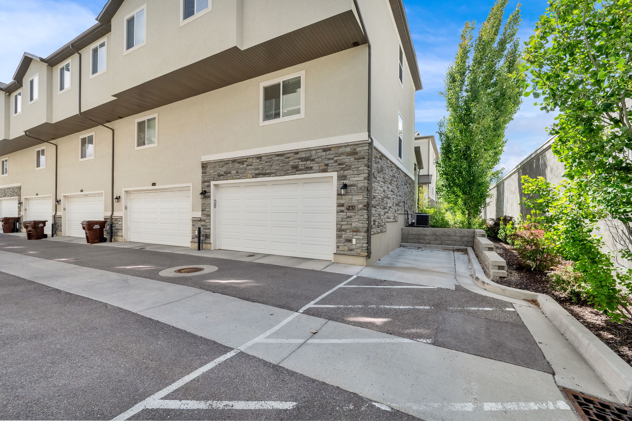 Townhome exterior featuring stucco siding with stone veneer accents, multiple white garage doors, and a paved driveway with marked parking spaces