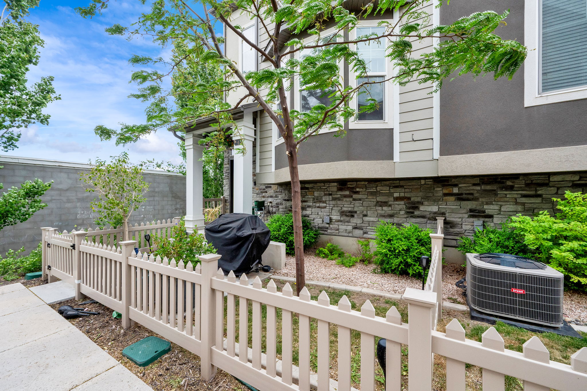 Compact fenced yard space featuring a picket fence, concrete pathway, and mature tree