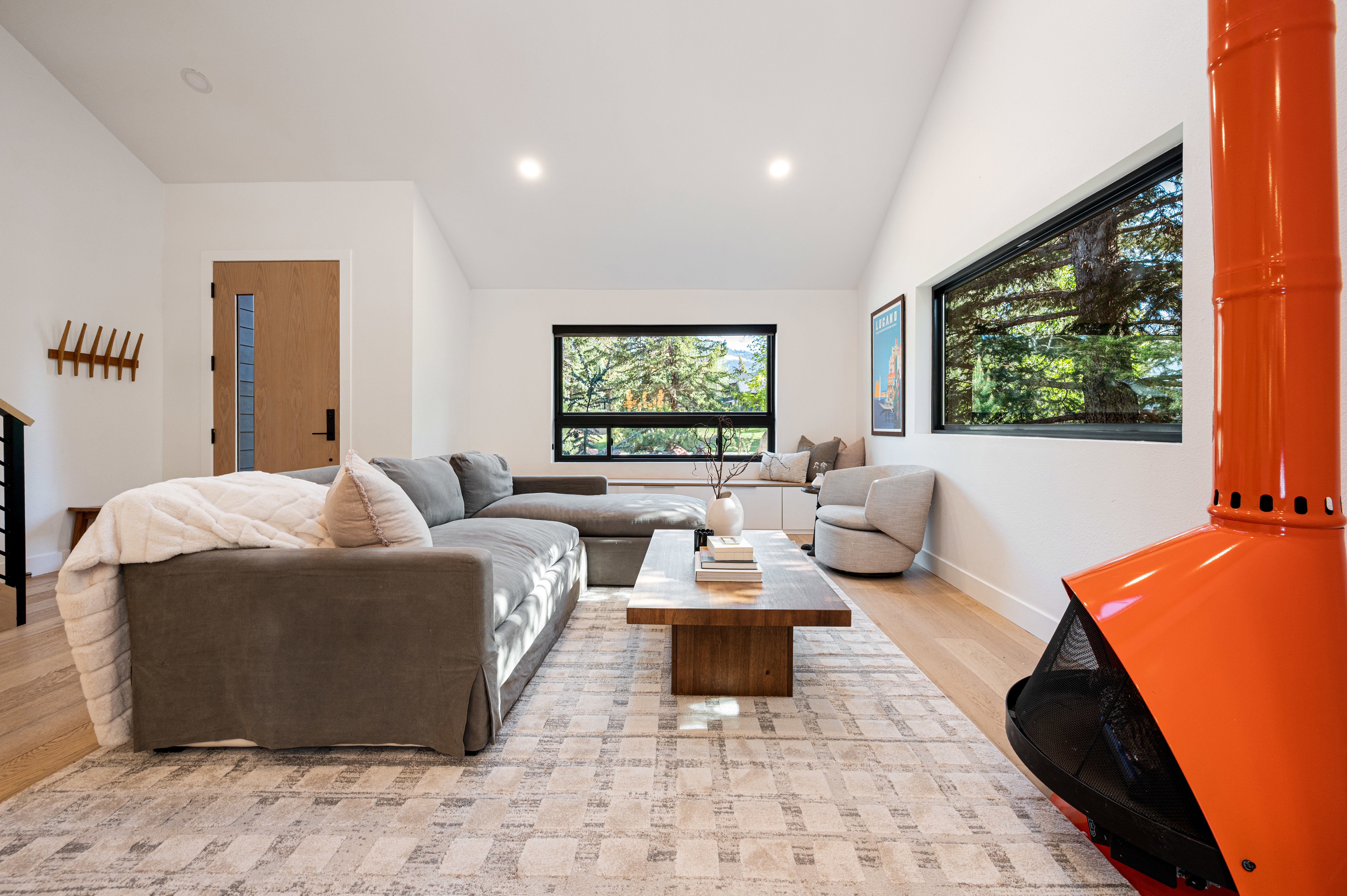Bright living area featuring a freestanding orange fireplace, blonde wood-finish flooring, recessed lighting, and multiple black-framed windows