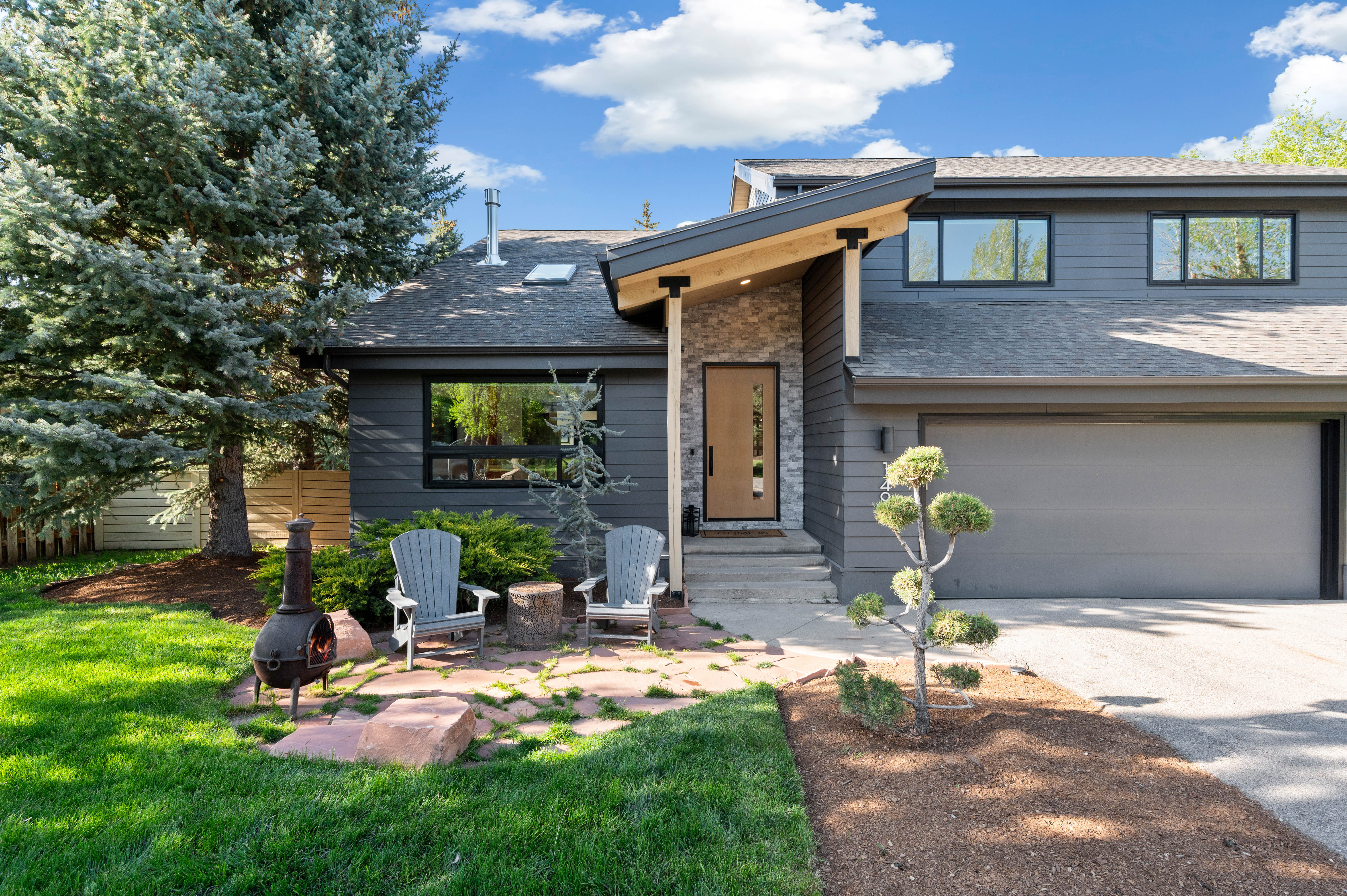 Contemporary exterior featuring dark gray siding and a light wood-clad entry porch with stone veneer accents