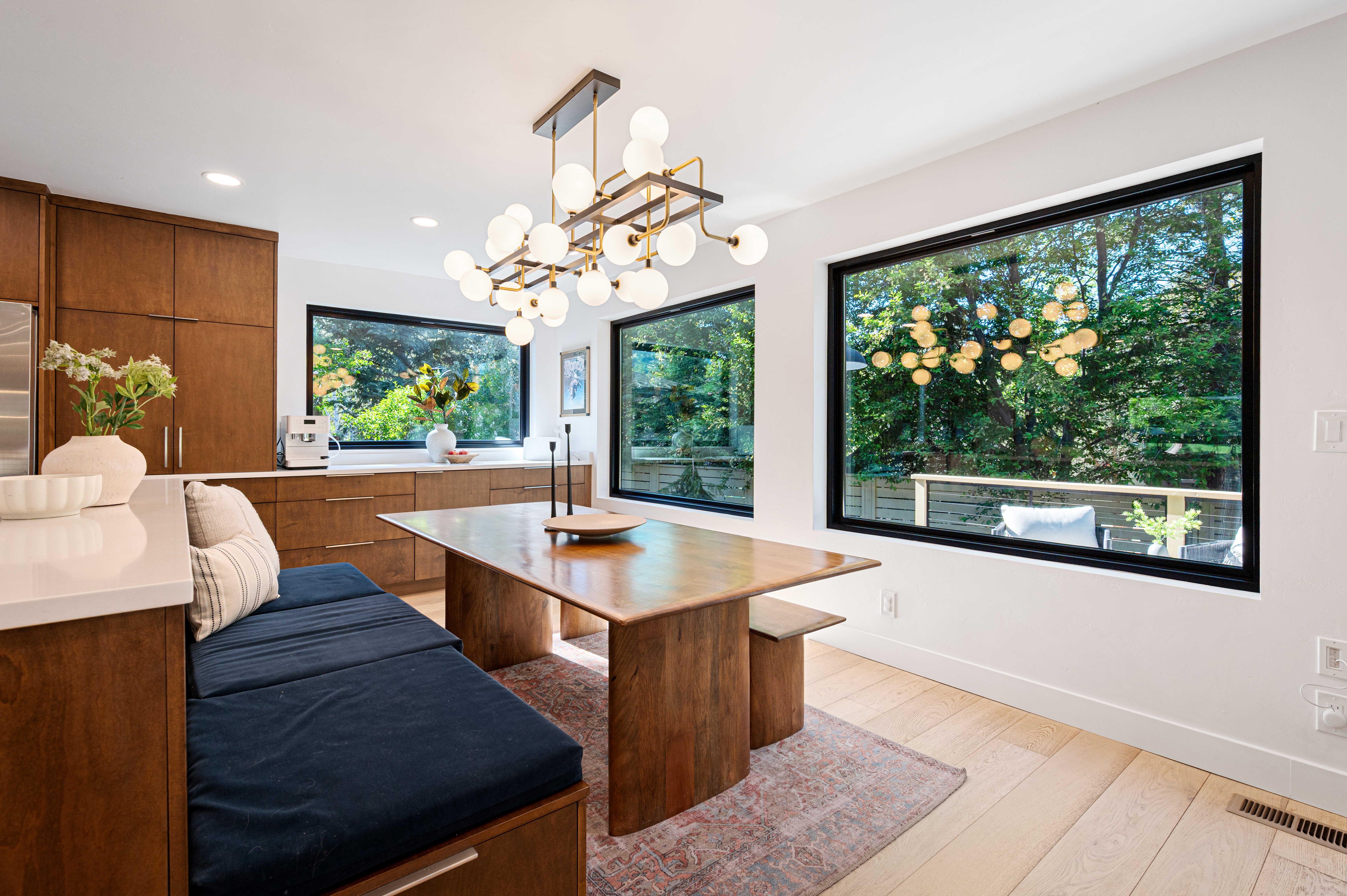 Modern kitchen and dining area featuring light wood-finish flooring, a contemporary chandelier, and a built-in banquette with storage
